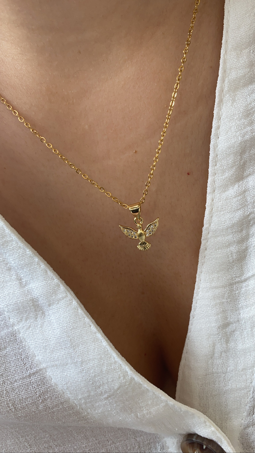 Colar dourado com pendente de pássaro usado sobre camisa branca