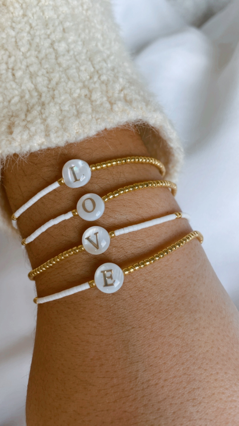 Pulseiras com letras brancas formando LOVE num pulso, com camisola creme felpuda ao fundo