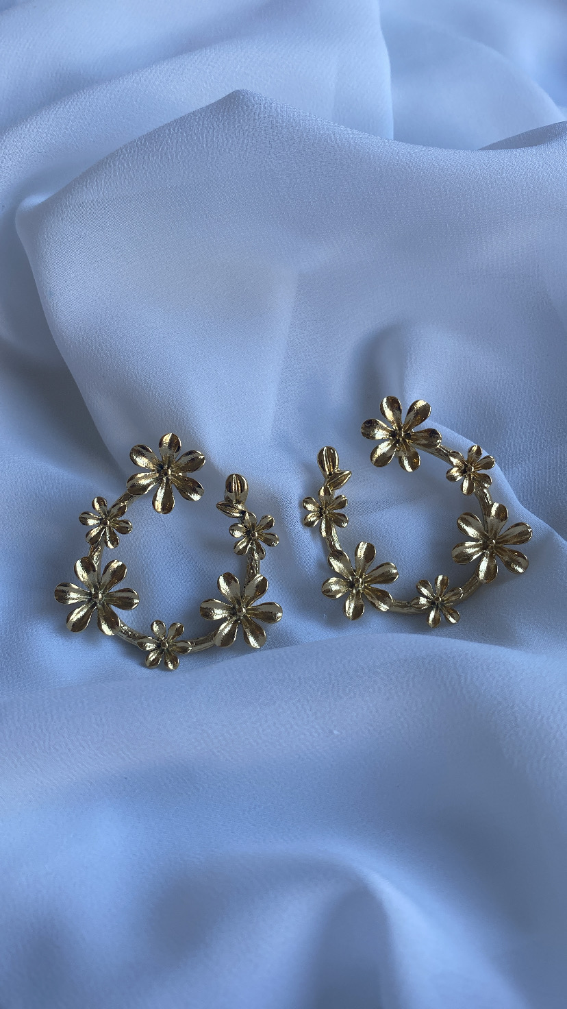 Brincos dourados em forma de flores sobre tecido branco