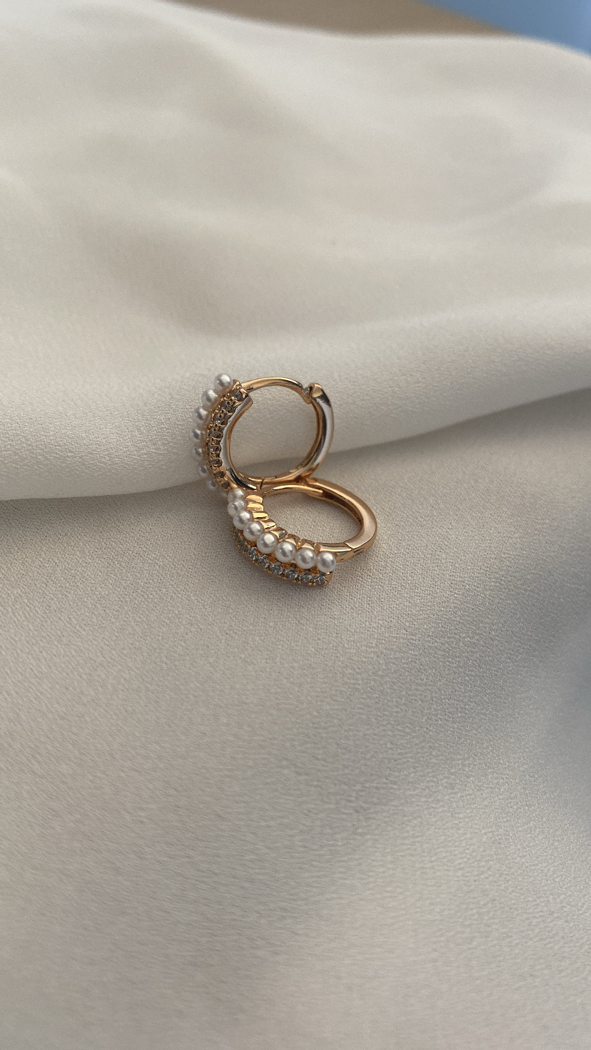 Par de argolas douradas com pérolas e cristais sobre tecido bege