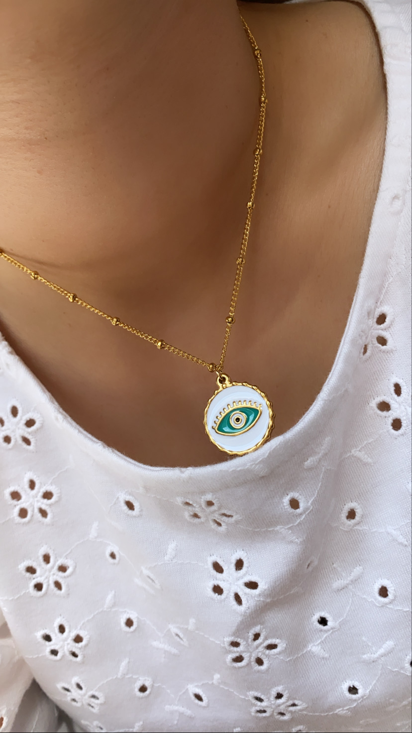 Colar dourado com pendente redondo de olho estilizado em blusa branca bordada