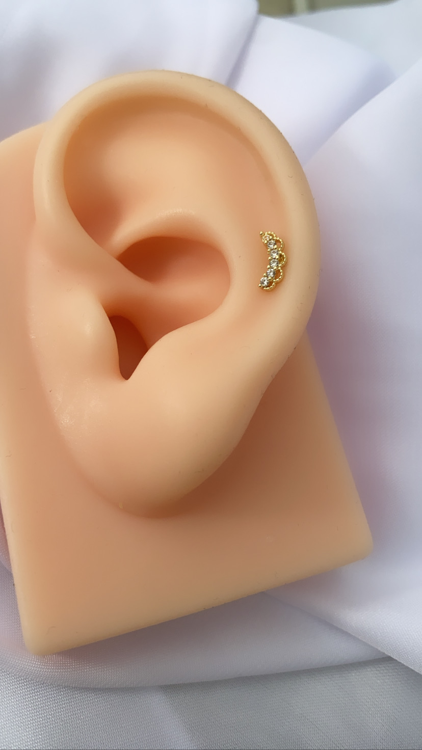 Brinco dourado com pedras em orelha de silicone sobre tecido branco