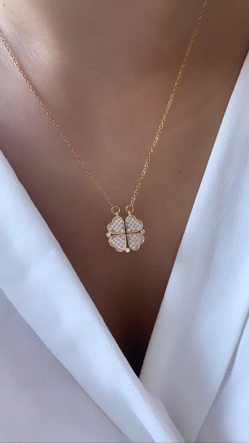 Colar dourado com pendente de trevo com brilhantes num pescoço com blusa branca