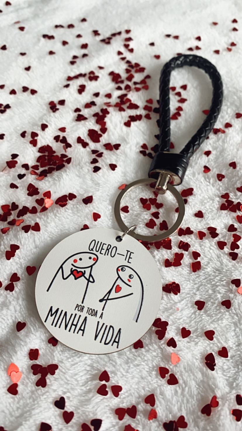 Porta-chaves redondo branco com desenho e texto em português e pega preta sobre superfície com confetes em forma de coração