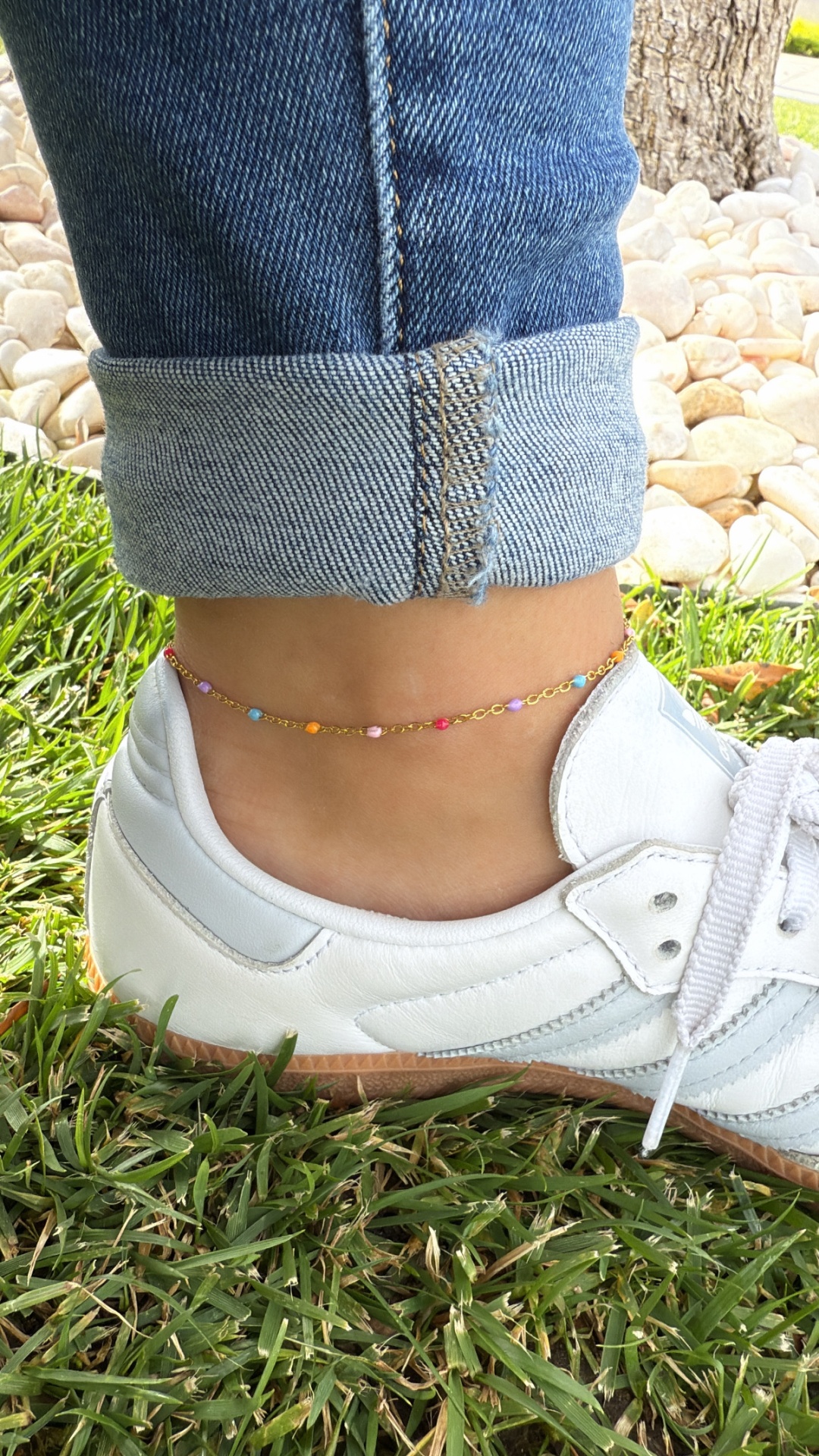 Tornozelo com pulseira colorida, calça de ganga azul e sapatilha branca em relvado