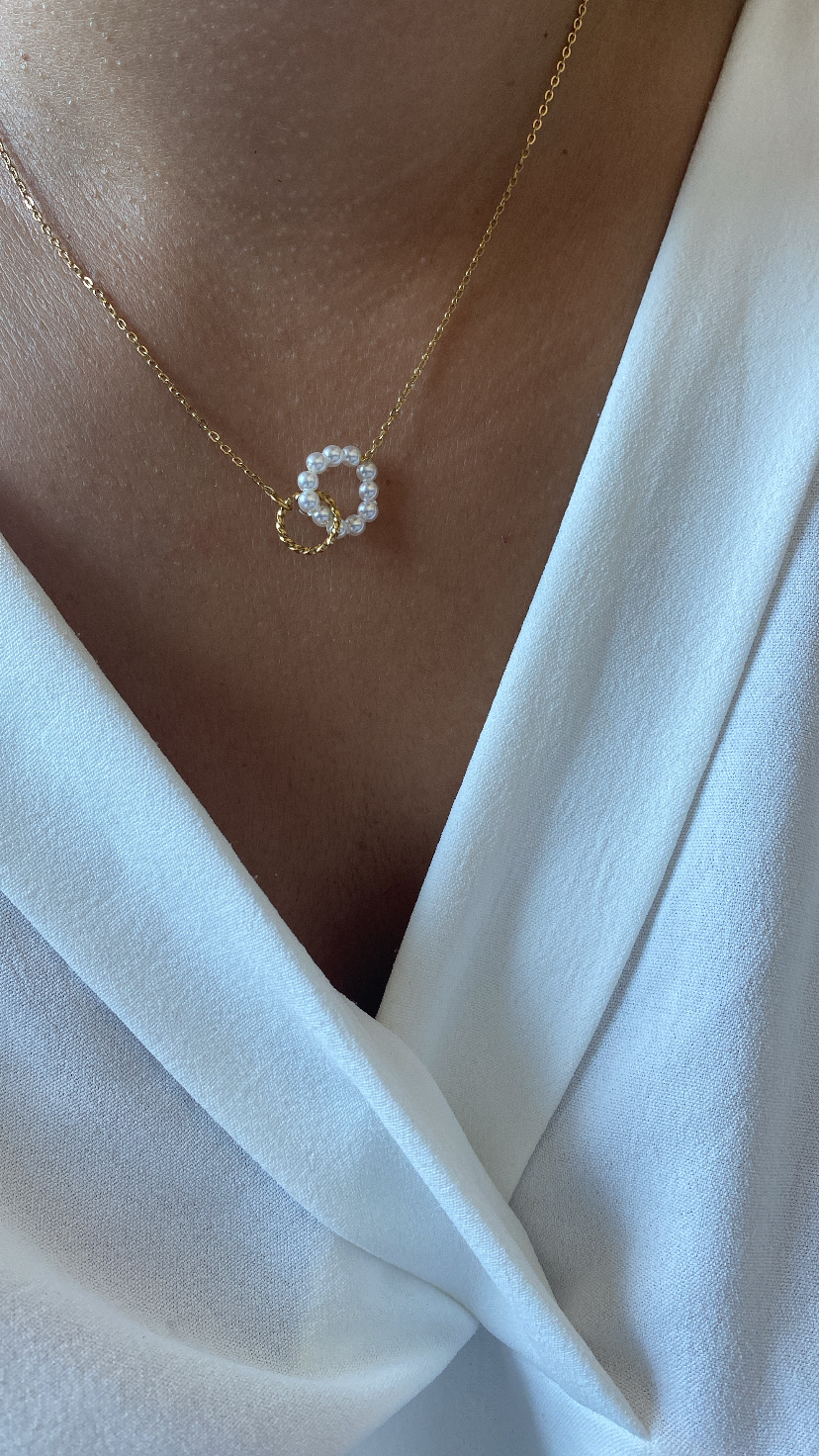 Colar dourado com pendentes de pérolas e metal, usado com camisa branca.