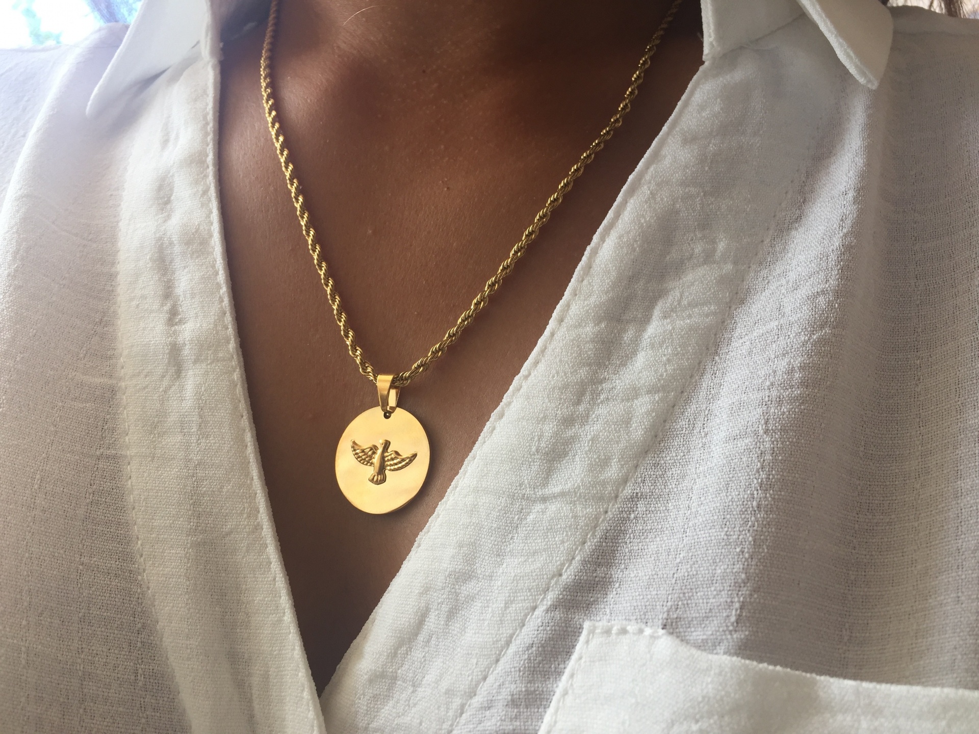Colar dourado com pendente redondo com símbolo de inseto numa camisa branca de linho.