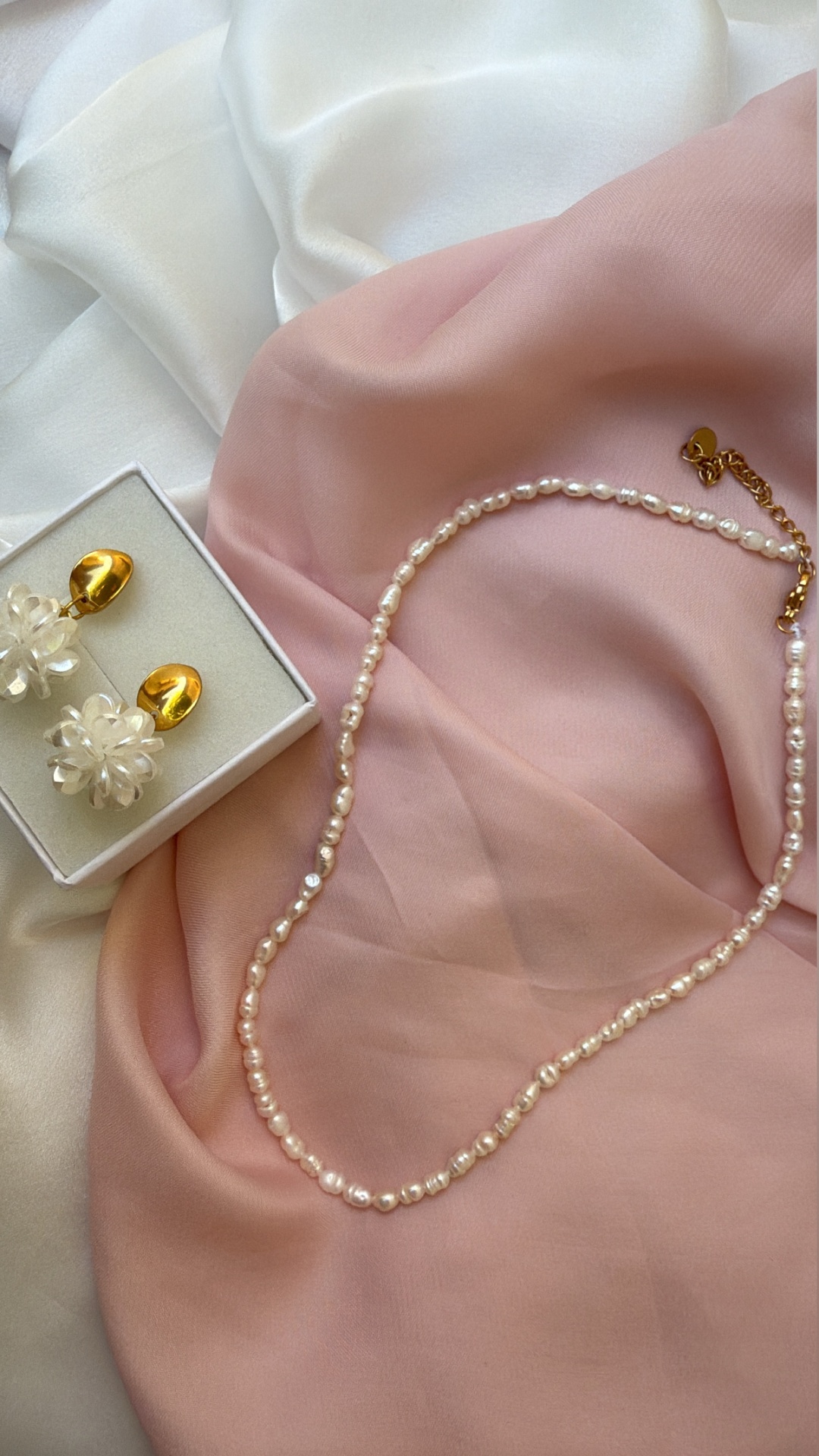 Colar de pérolas e brincos dourados com flores transparentes sobre tecidos branco e rosa