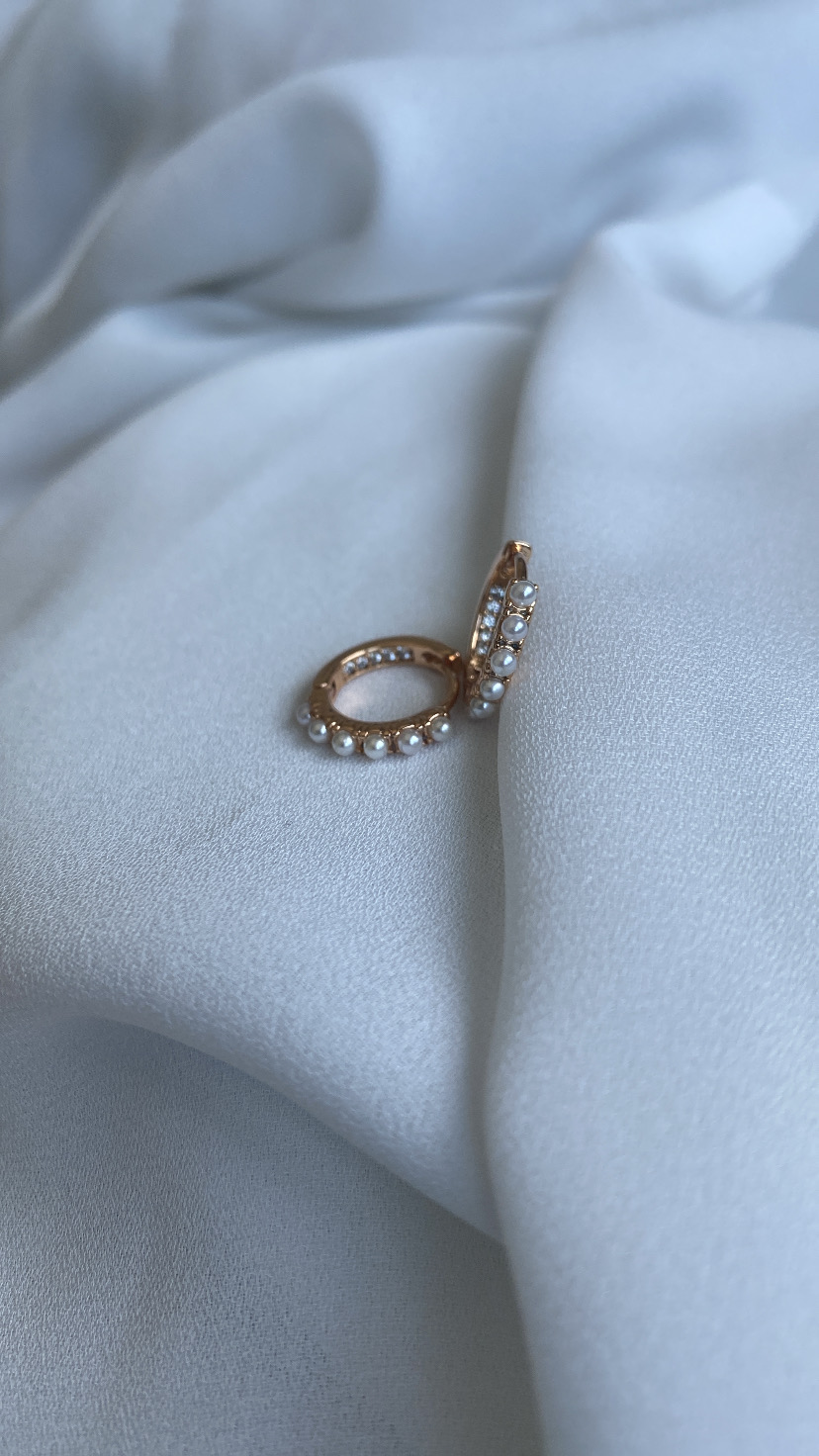 Brincos de argola dourados com pérolas sobre tecido branco