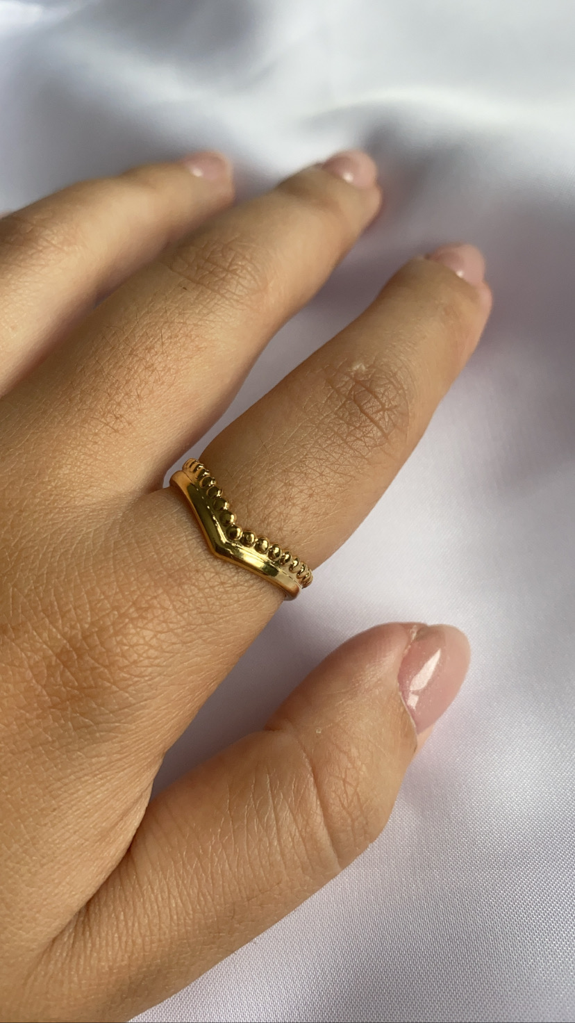 Anel dourado em V com bolinhas, mão feminina em tecido branco