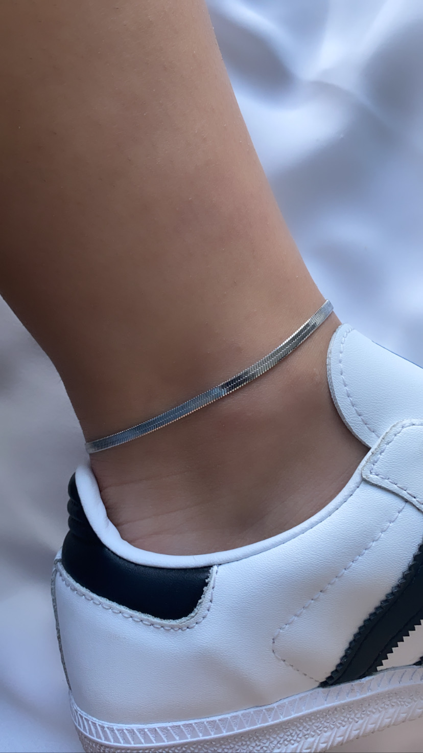 Pulseira fina no tornozelo e parte de ténis branco com detalhes a preto