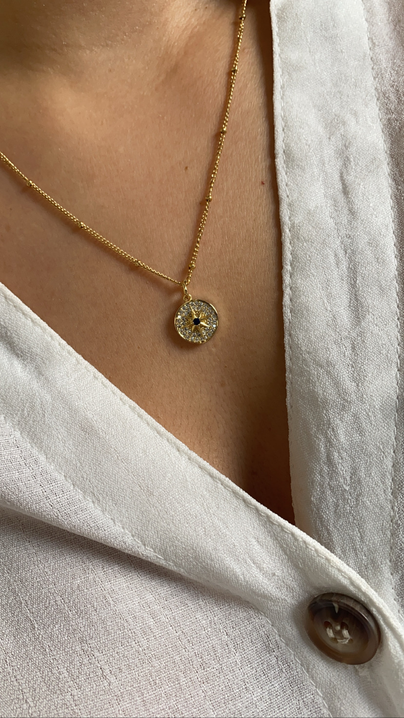 Colar dourado com pendente redondo de pedras e camisa branca