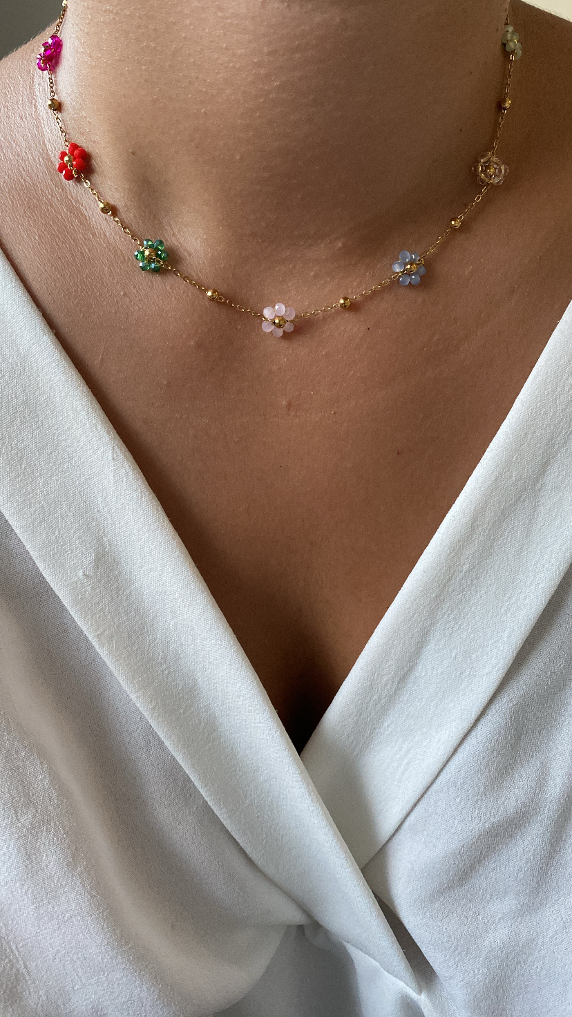 Colar dourado com flores coloridas num pescoço vestindo camisola branca