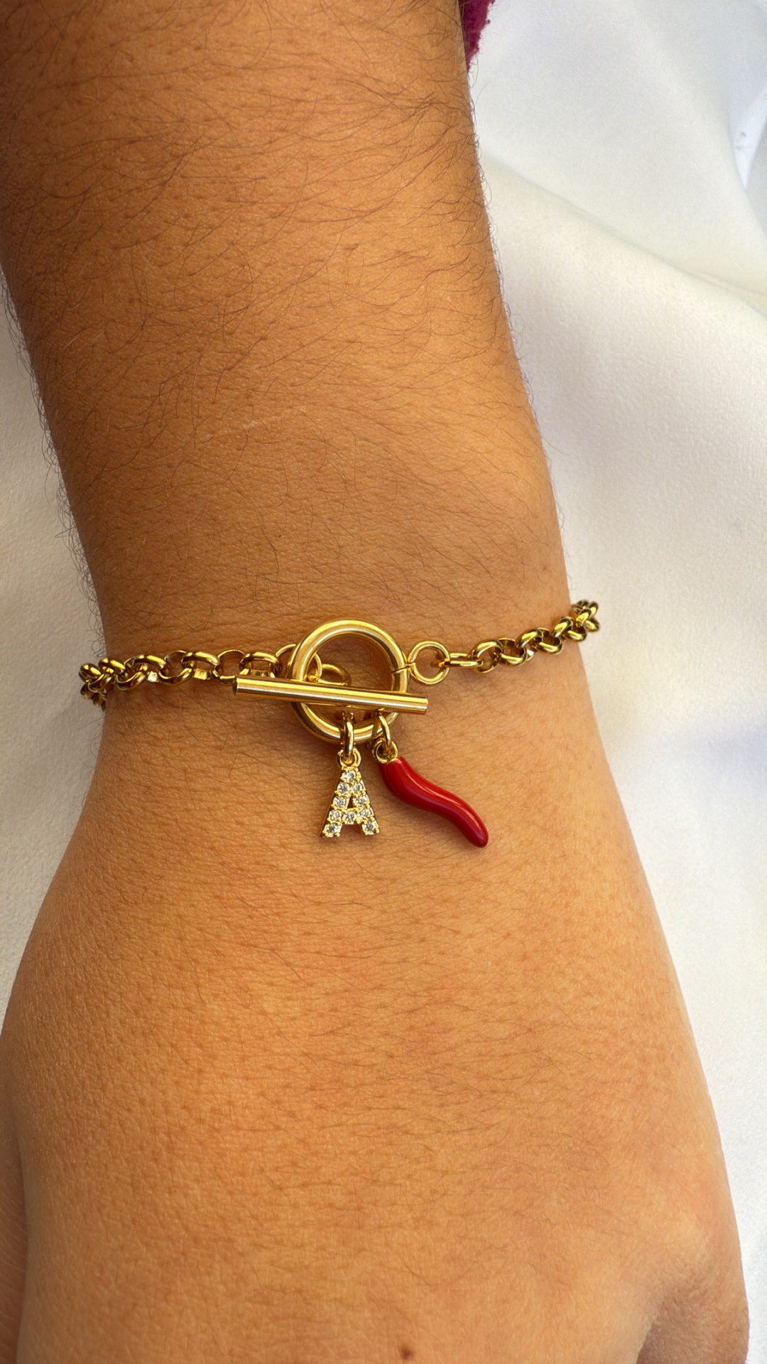 Pulseira dourada com pendentes vermelho e letra A num pulso