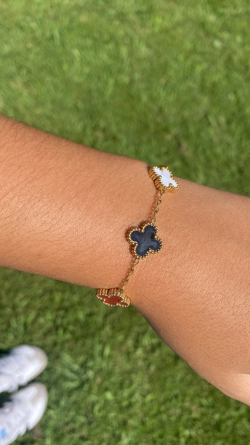Pulseira dourada com pingentes em forma de trevo em branco, preto e castanho ao pulso