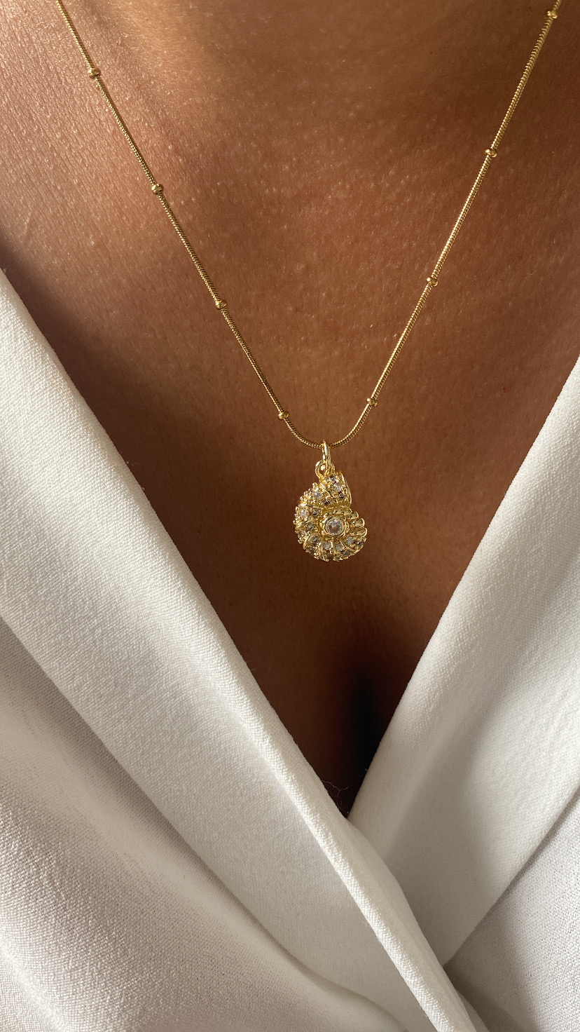 Colar dourado com pendente espiral e cristais sobre pele e roupa branca