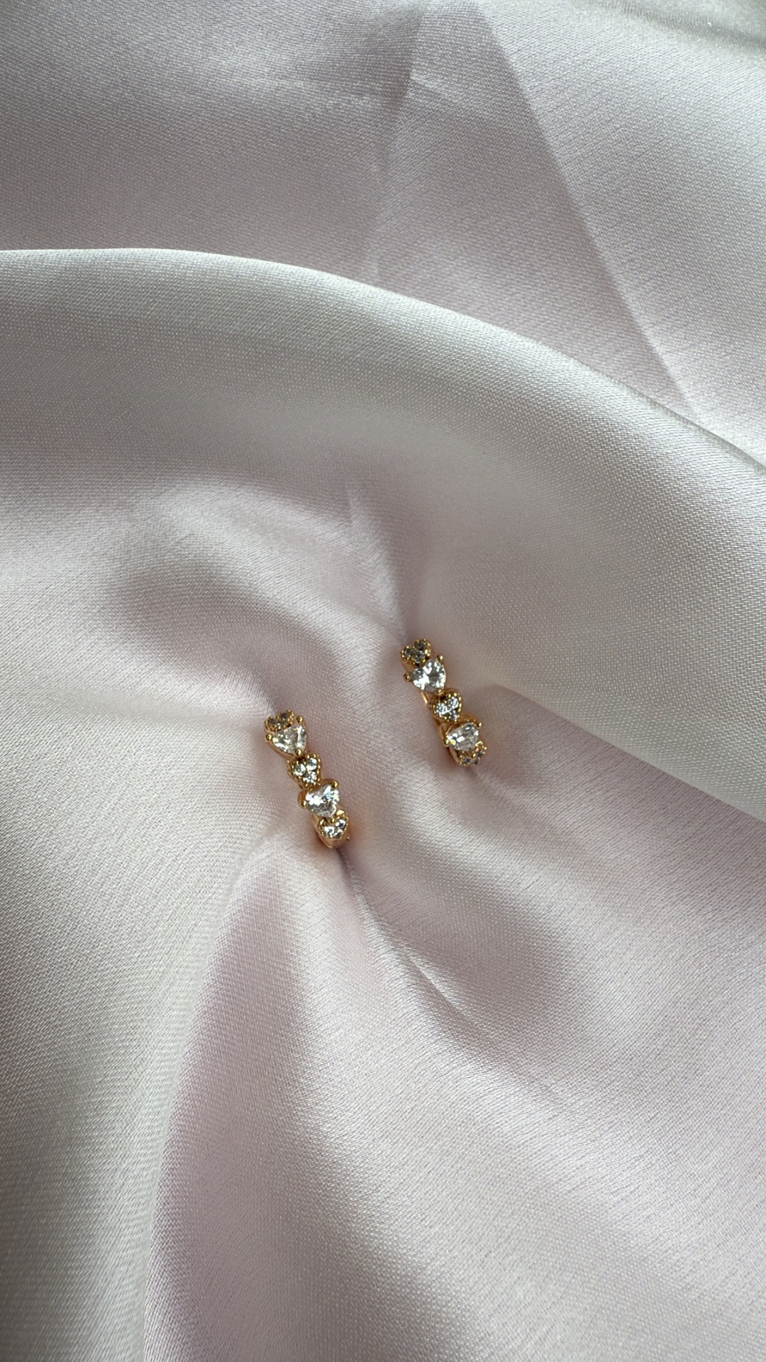 Brincos dourados com pedras transparentes sobre tecido branco acetinado
