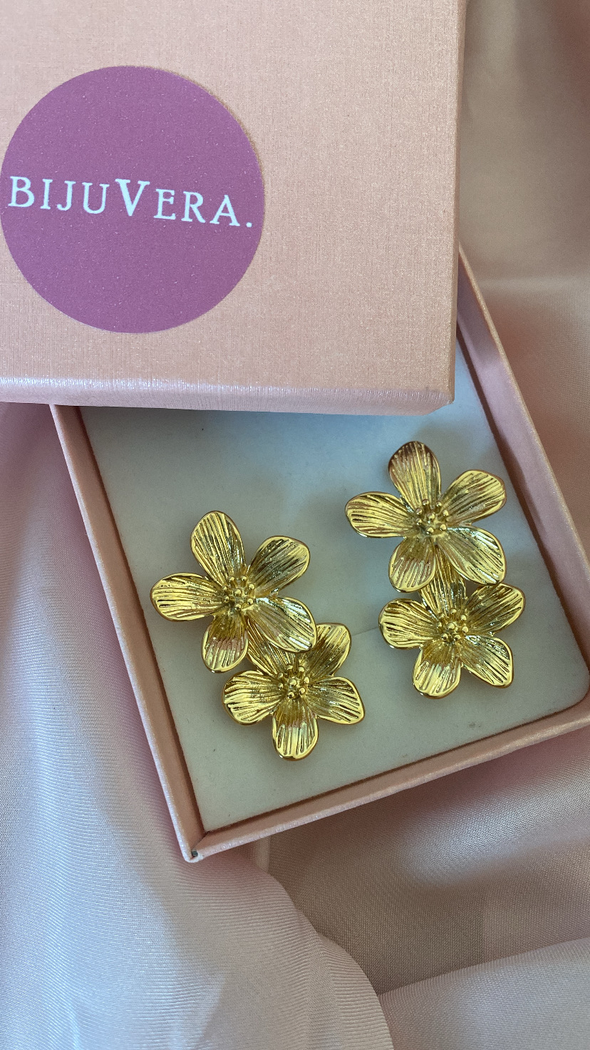 Brincos dourados em forma de flores em caixa de joias rosa.