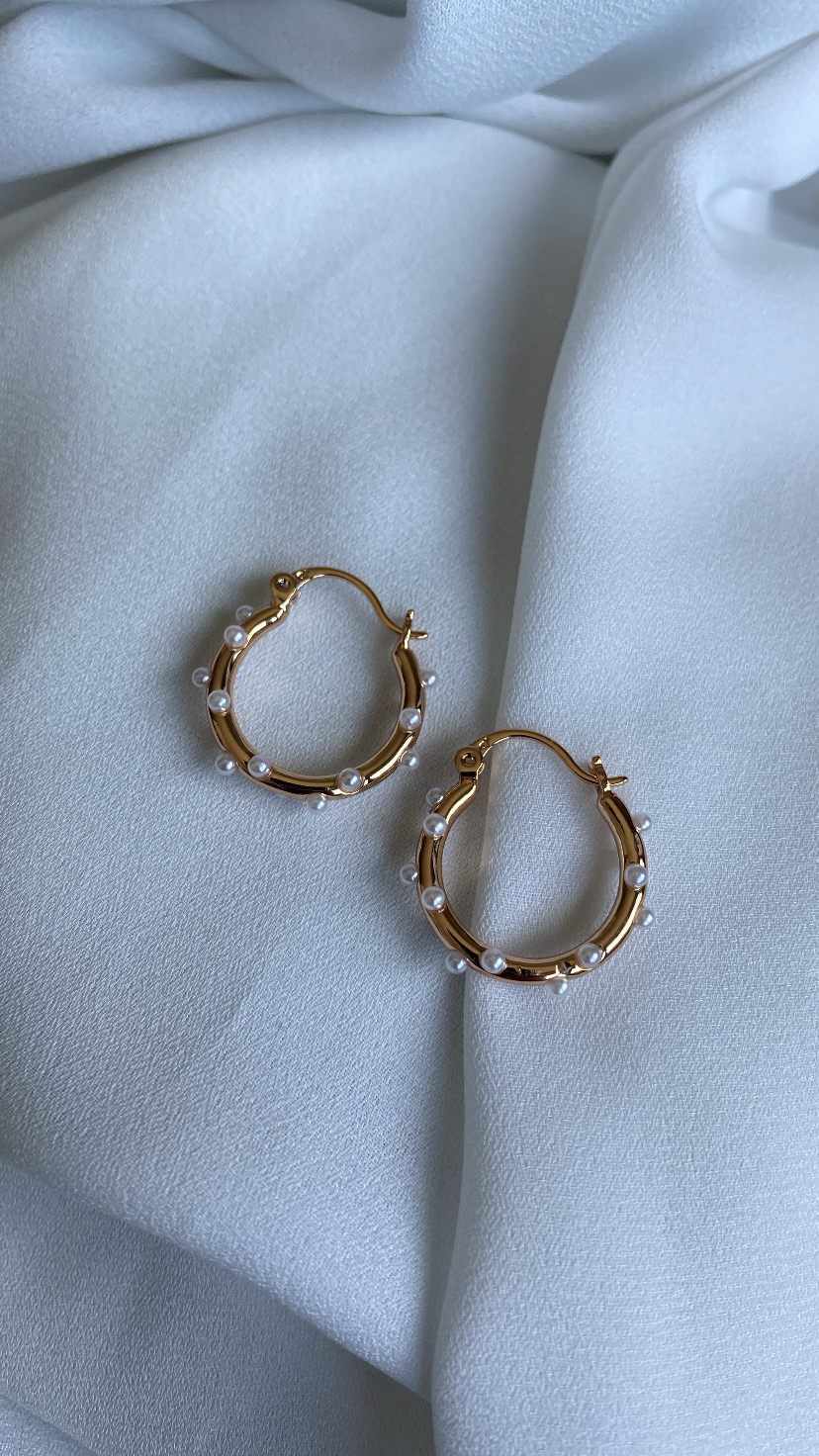 Brincos argola dourados com pérolas sobre tecido branco