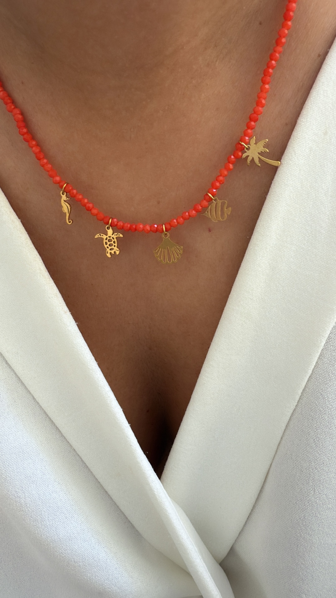 Colar com contas vermelhas e pendentes dourados em forma de animais e plantas