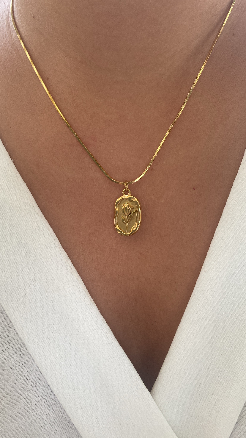 Colar dourado com pendente floral em relevo sobre camisa branca