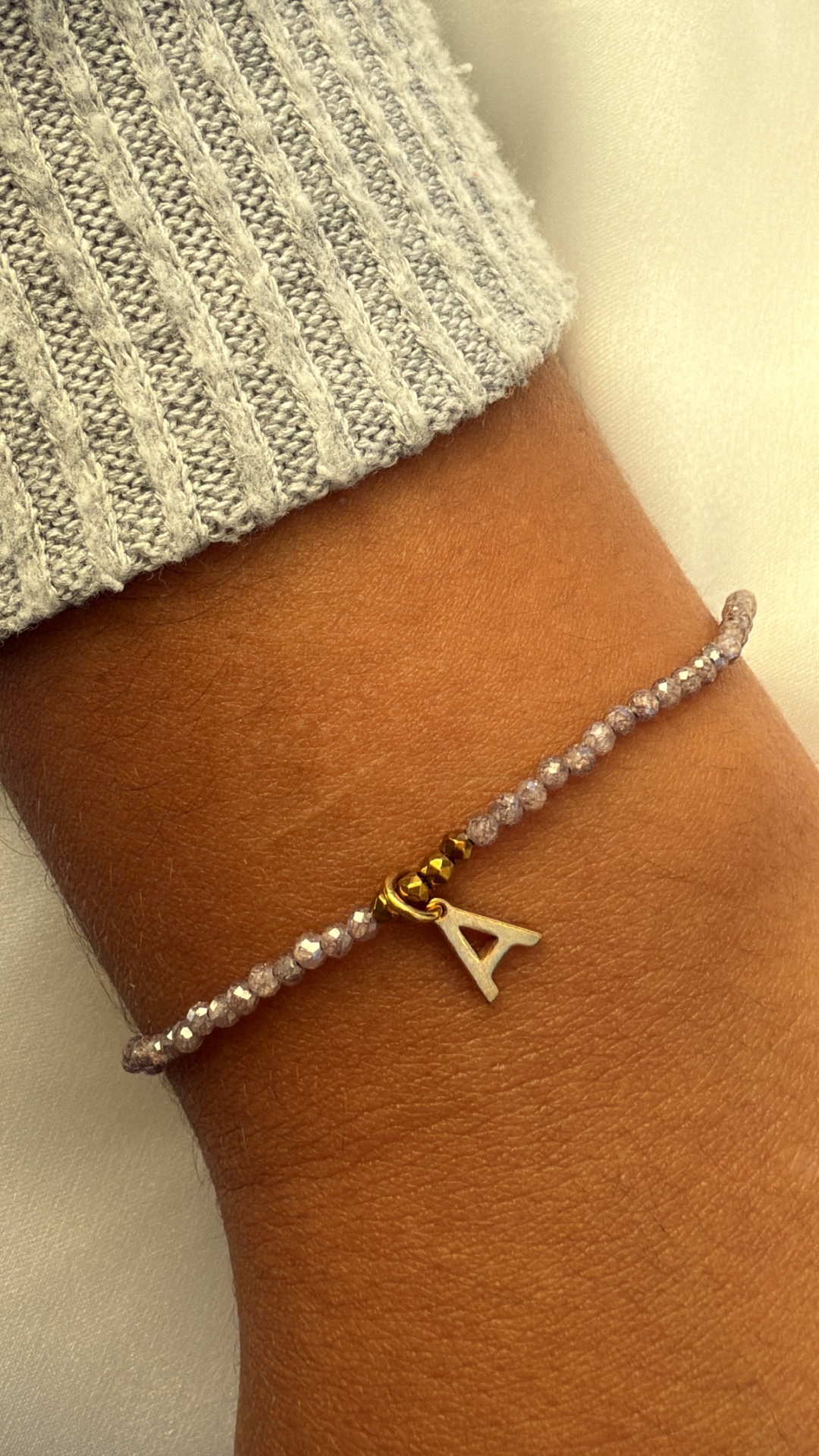 Pulseira com contas cinzentas e pendente letra A no pulso