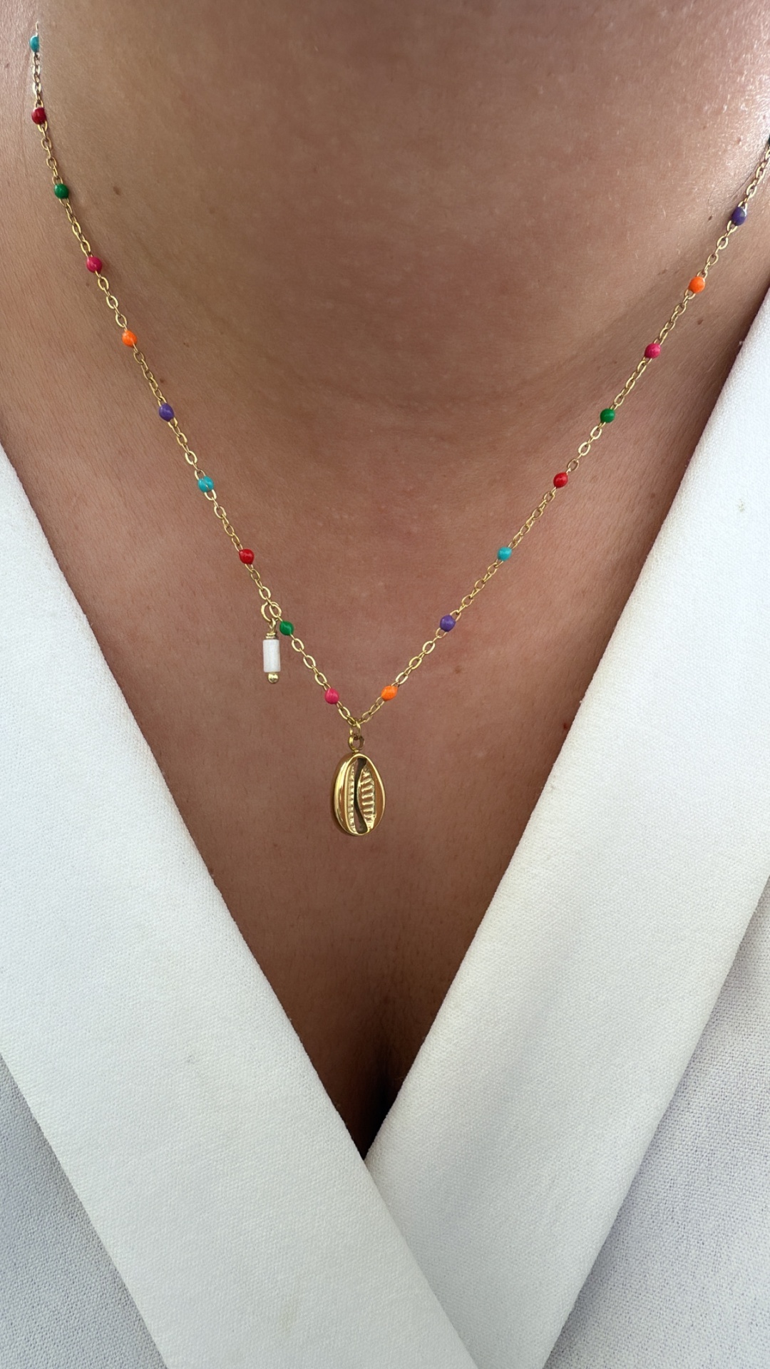 Colar dourado com contas coloridas e pingente de concha sobre roupa branca
