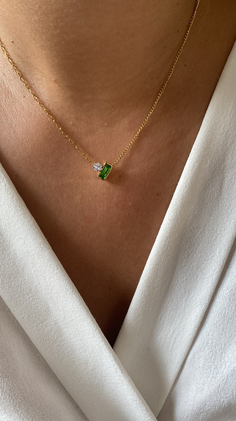 Colar dourado com pendente verde e pedra clara num peito com vestido branco