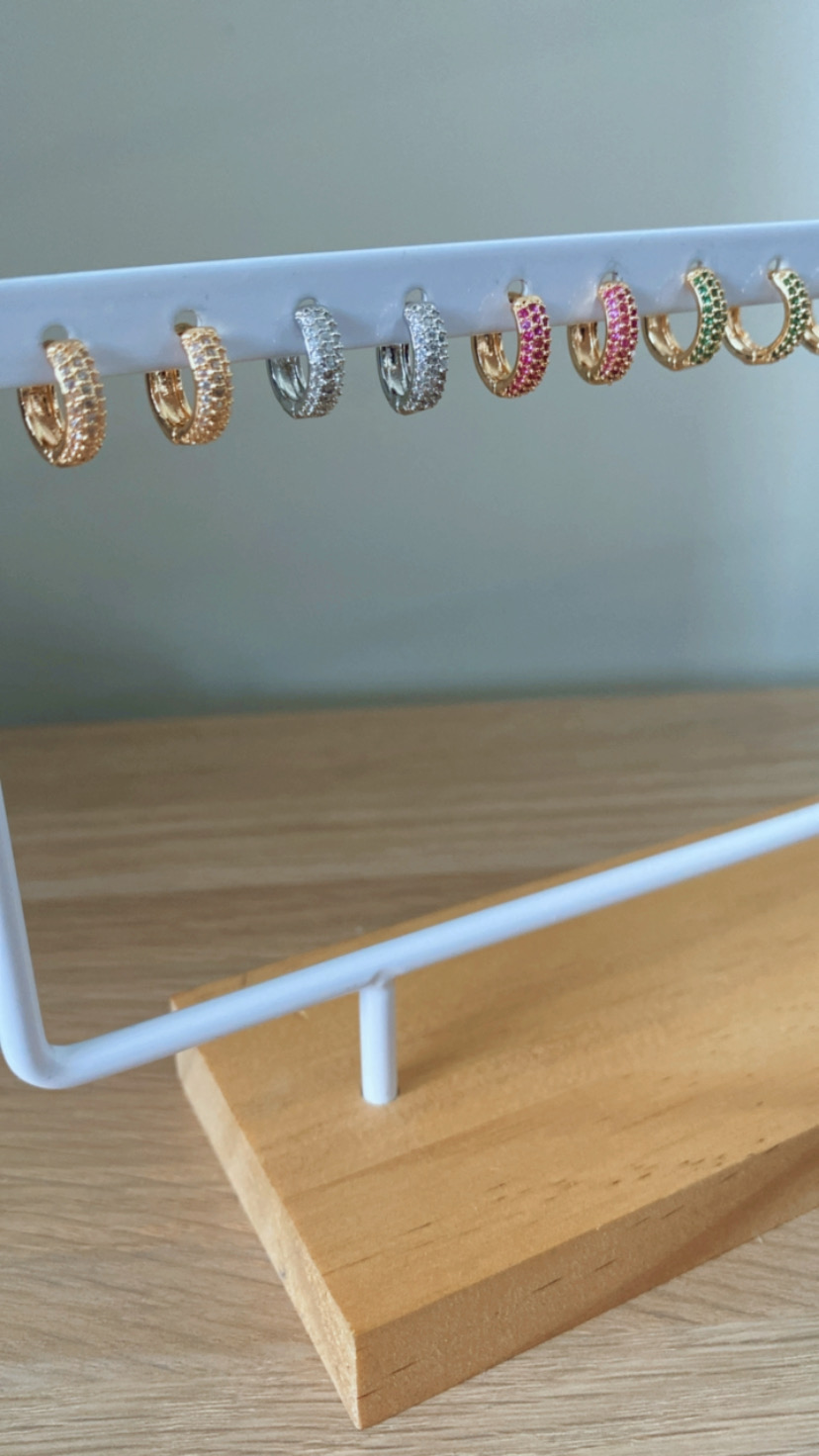 sete pares de brincos argola pequenos com pedras coloridas num suporte branco com base de madeira