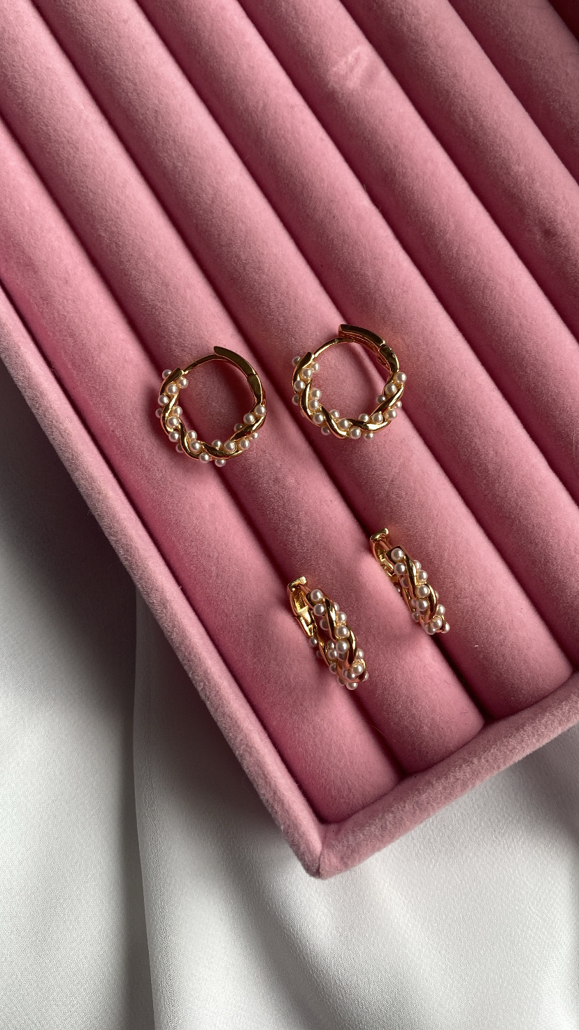 Conjunto de brincos dourados com pérolas numa caixa de veludo rosa.