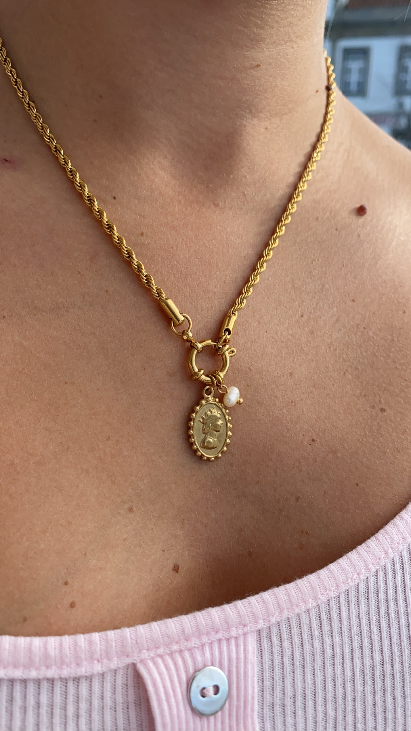 Colar dourado com pendente oval e pérola, usado com camisola cor-de-rosa claro