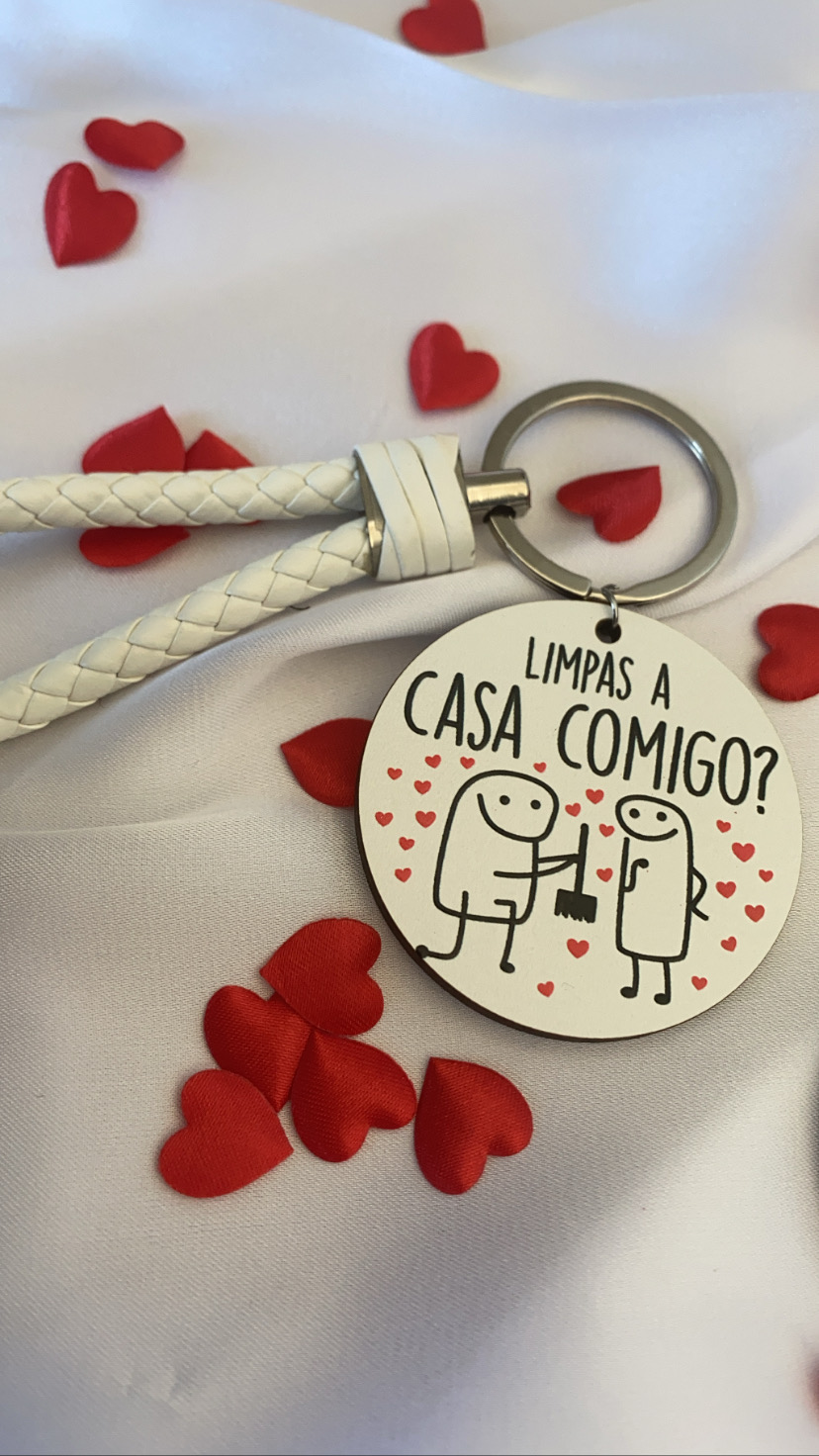 Chaveiro redondo com ilustração e texto em português sobre limpar a casa, com suporte branco e corações vermelhos ao fundo