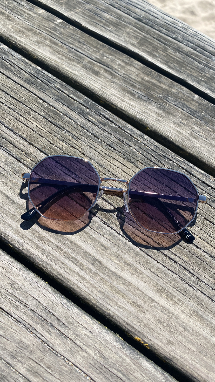 Óculos de sol metálicos com lentes azuis e roxas sobre madeira envelhecida