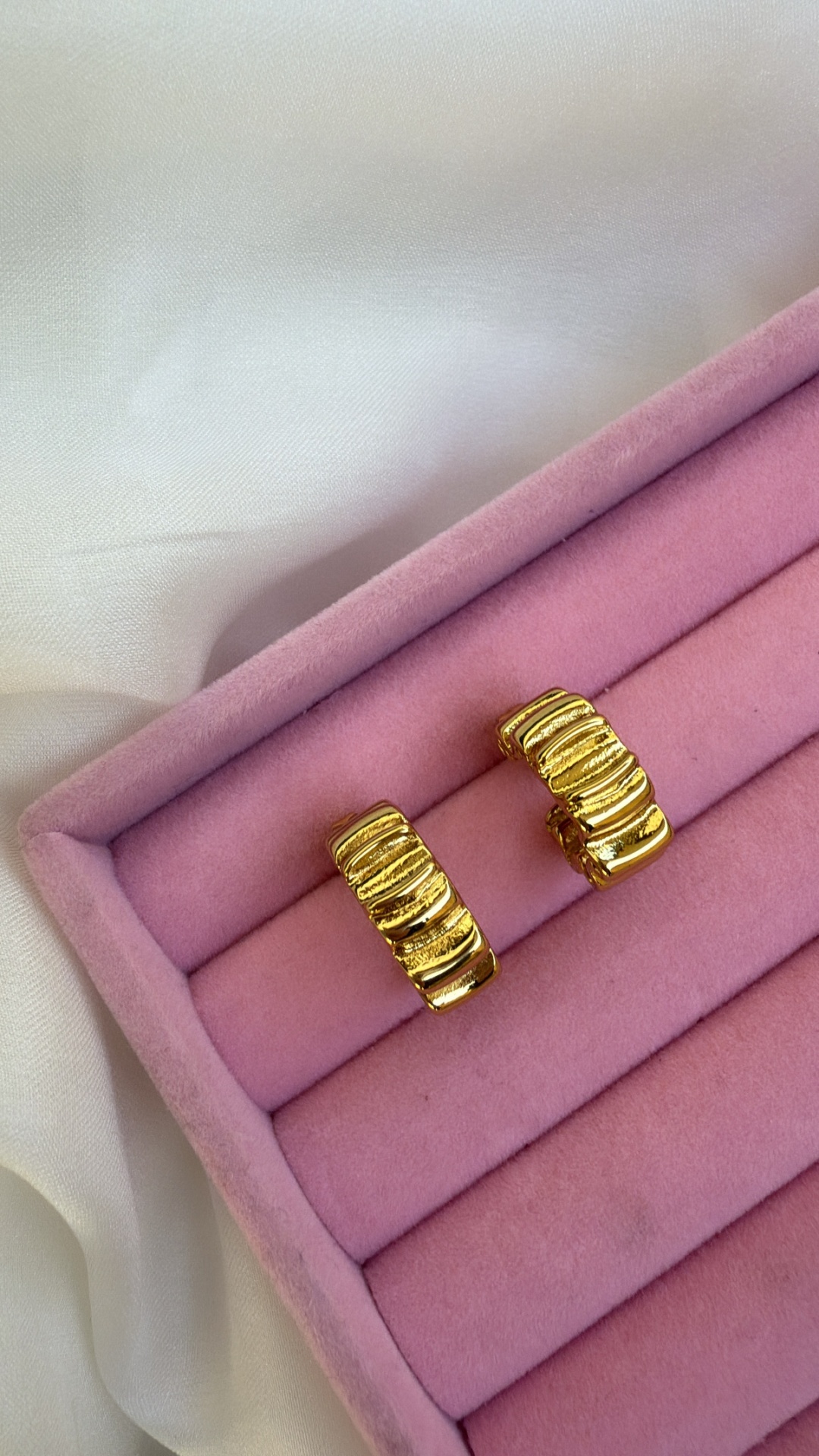 Brincos dourados ondulados numa caixa de veludo rosa