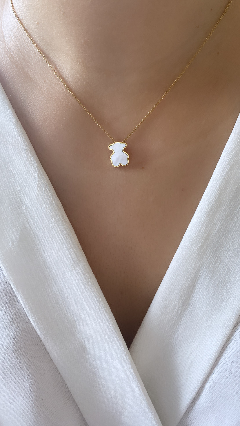 Colar com pendente de urso branco e corrente dourada em pescoço sobre blusa branca