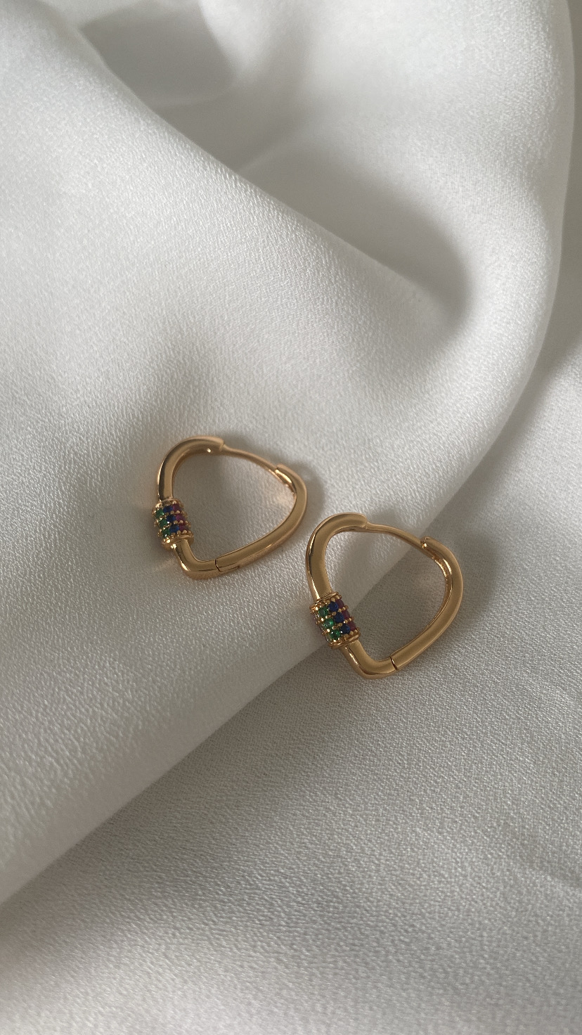 Brincos dourados em forma de coração com pedras coloridas sobre tecido branco