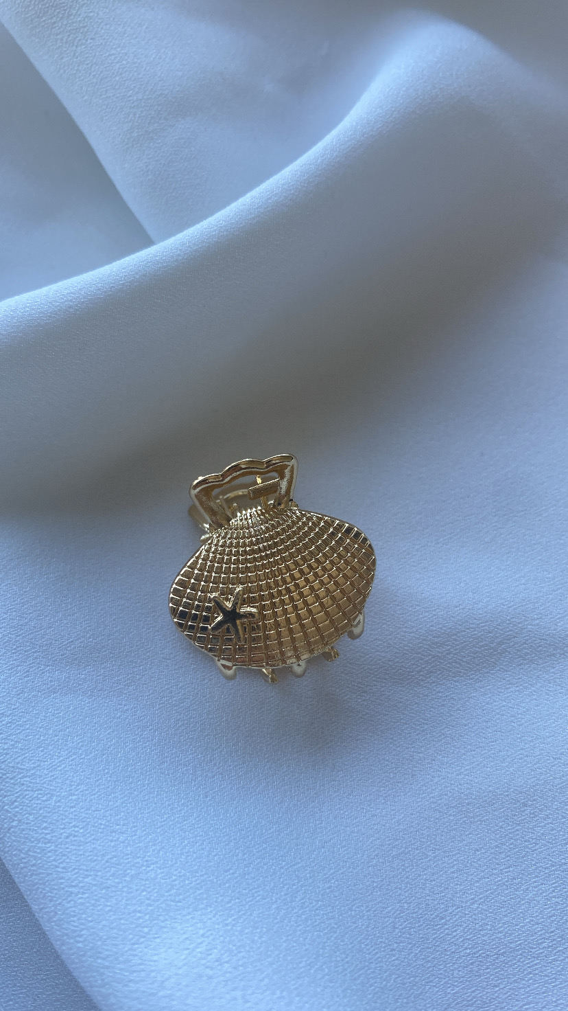 Presilha de cabelo dourada em forma de concha com estrela do mar sobre tecido branco