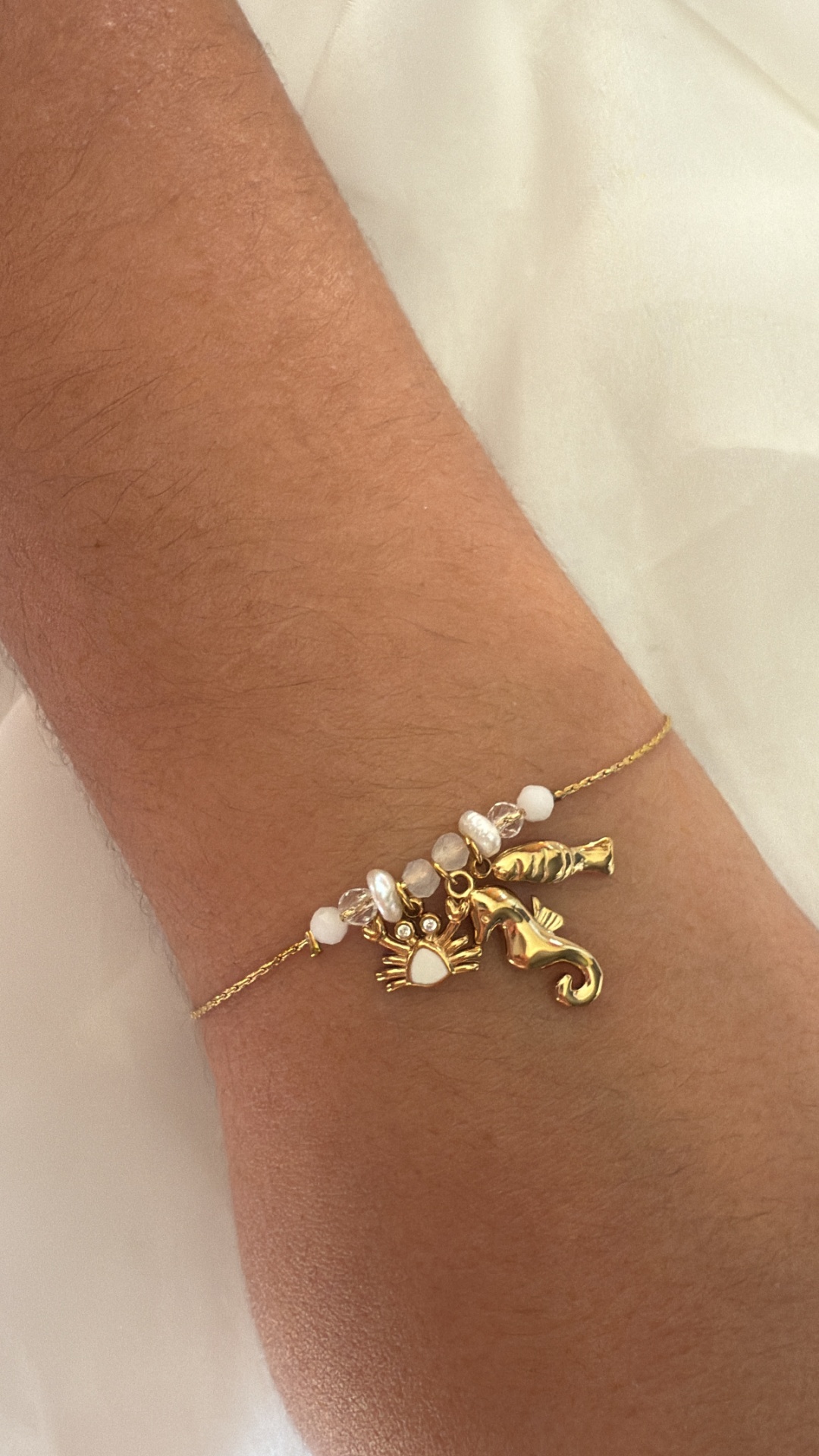 Pulseira dourada com pendentes de mariscos e pérolas no pulso