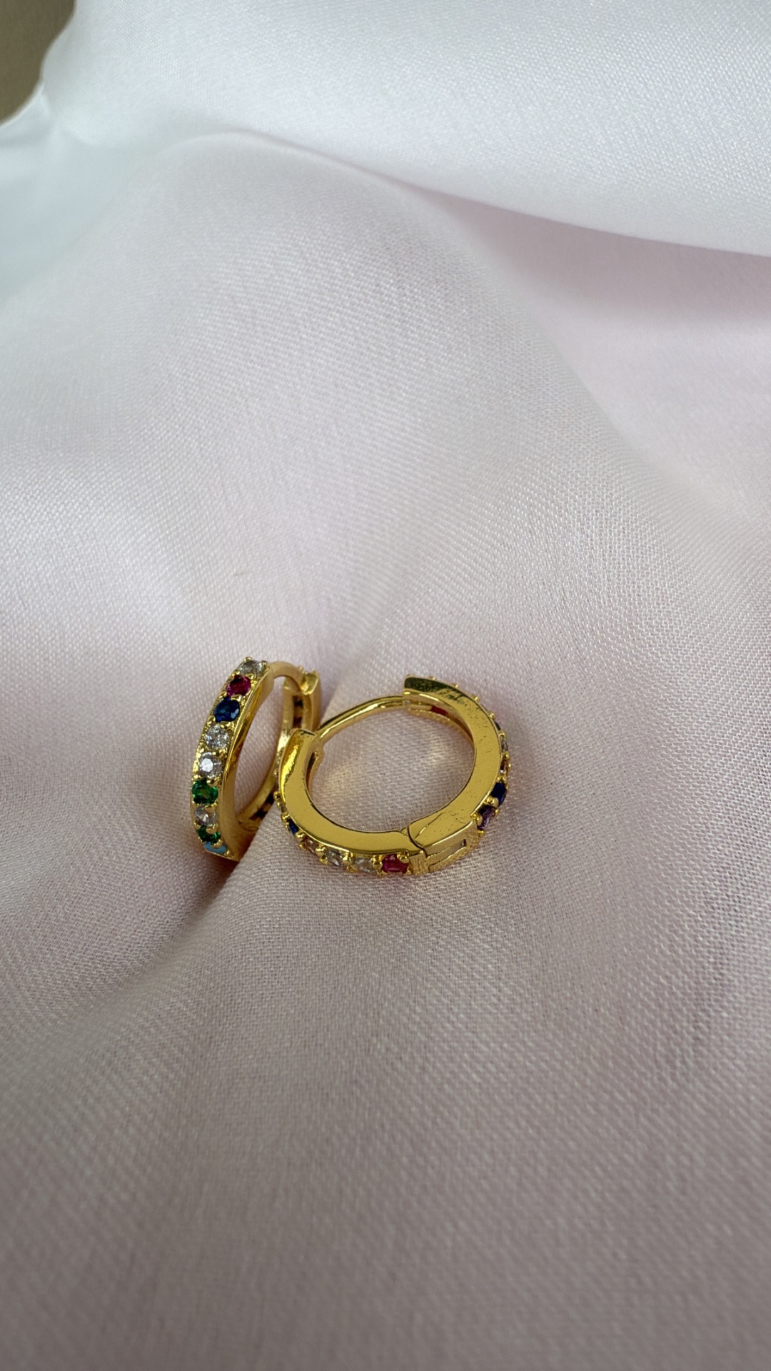 Brincos argola dourados com pedras coloridas sobre tecido branco