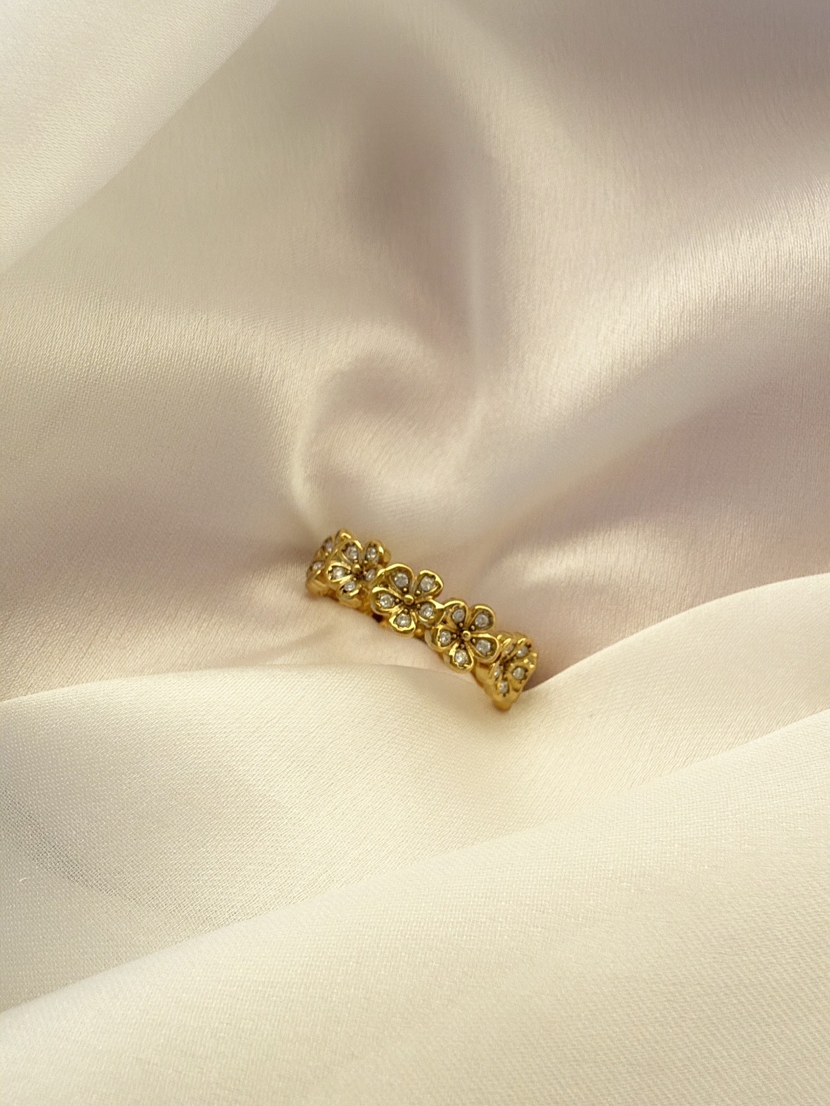 Anel de flores dourado com pedras sobre tecido creme