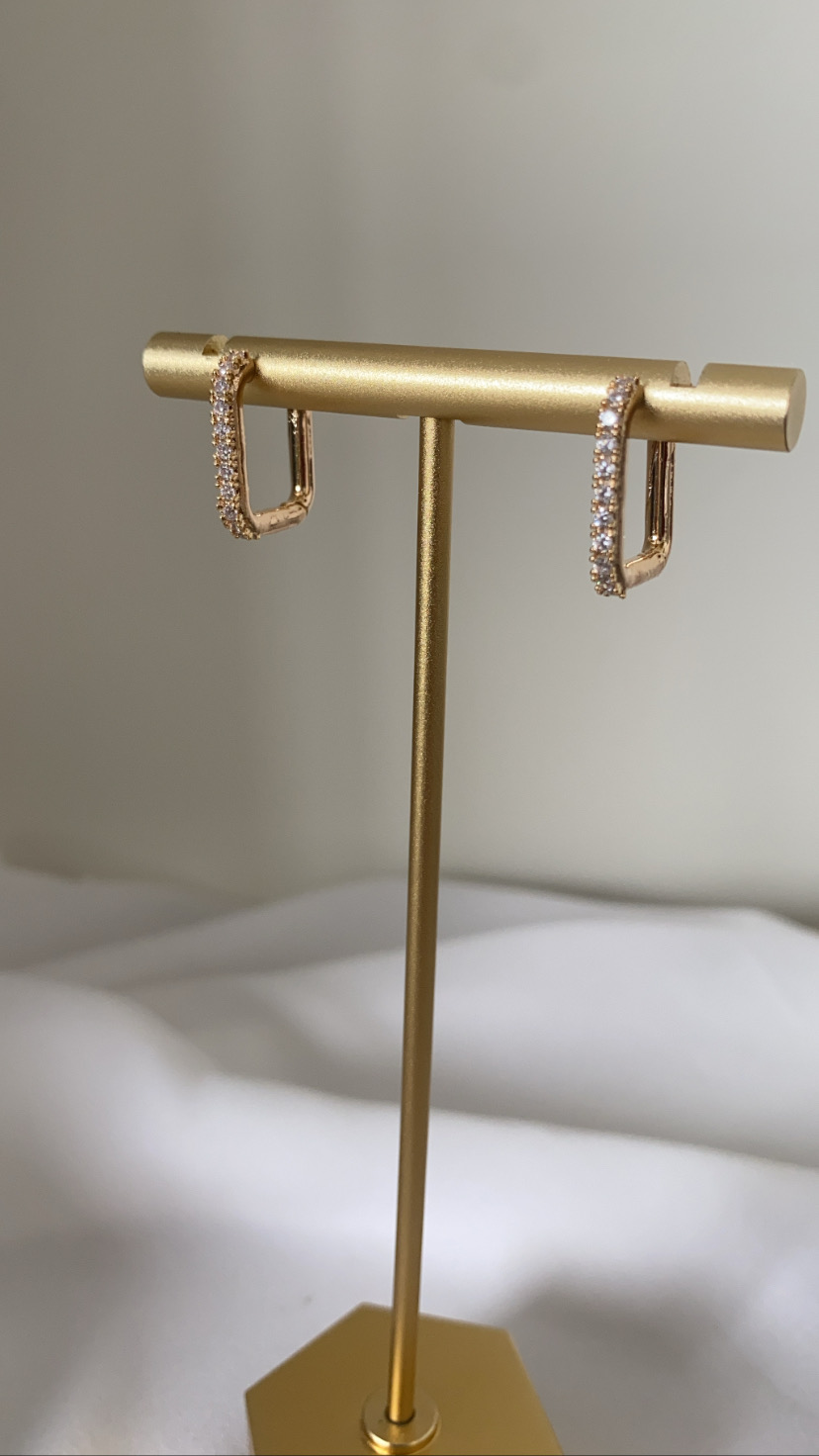 brincos dourados com pedras brilhantes num suporte metalico dourado