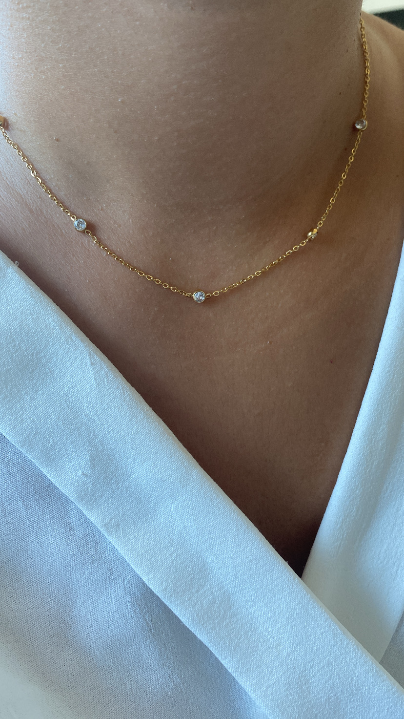 Colar dourado com pedras transparentes e camisa branca