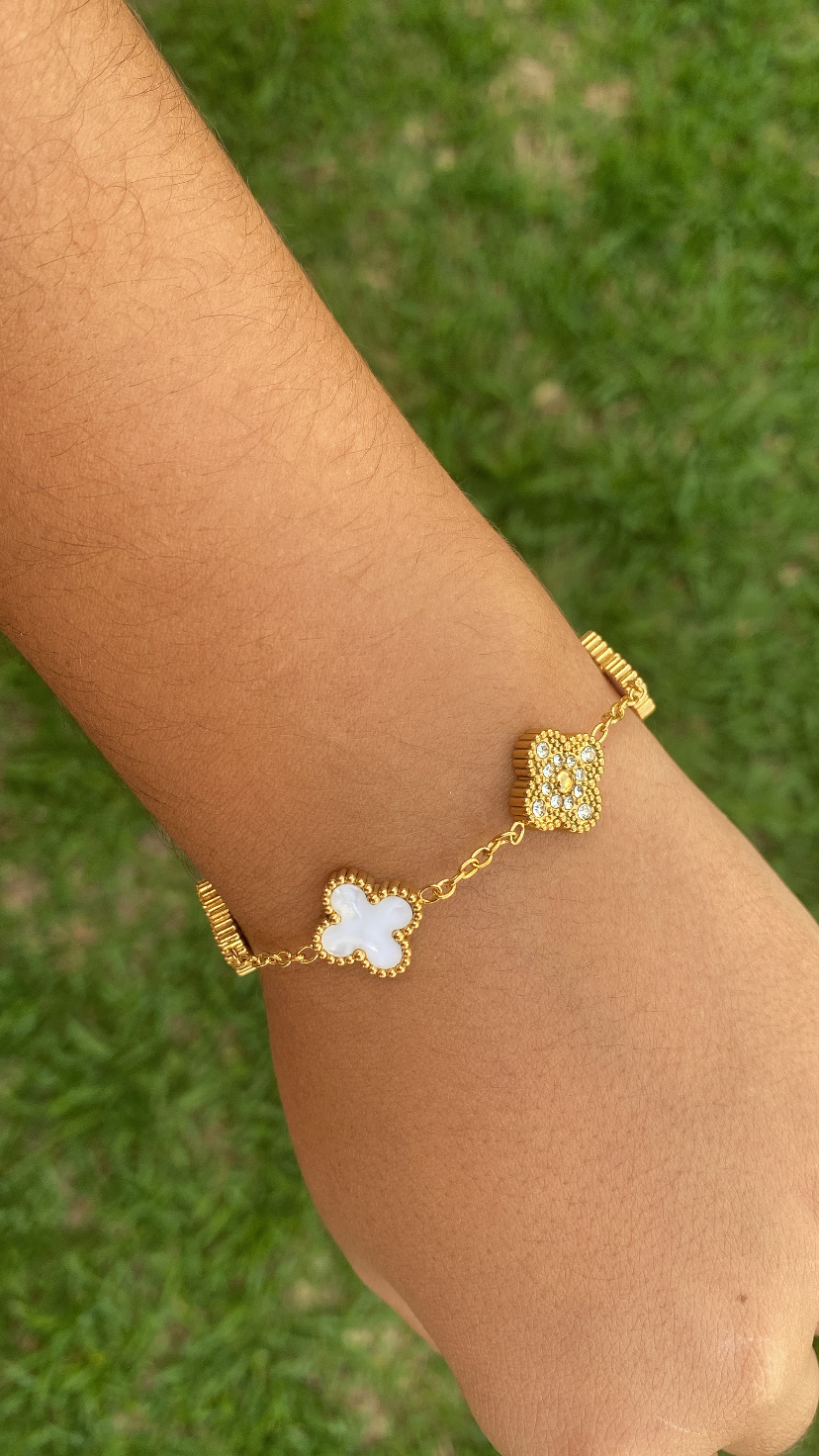 Pulseira dourada com flores branca e dourada com pedras em fundo verde