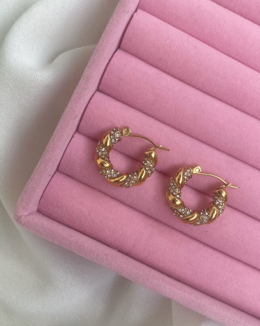 Brincos de argola dourados com pedras exibidos em estojo rosa acolchoado