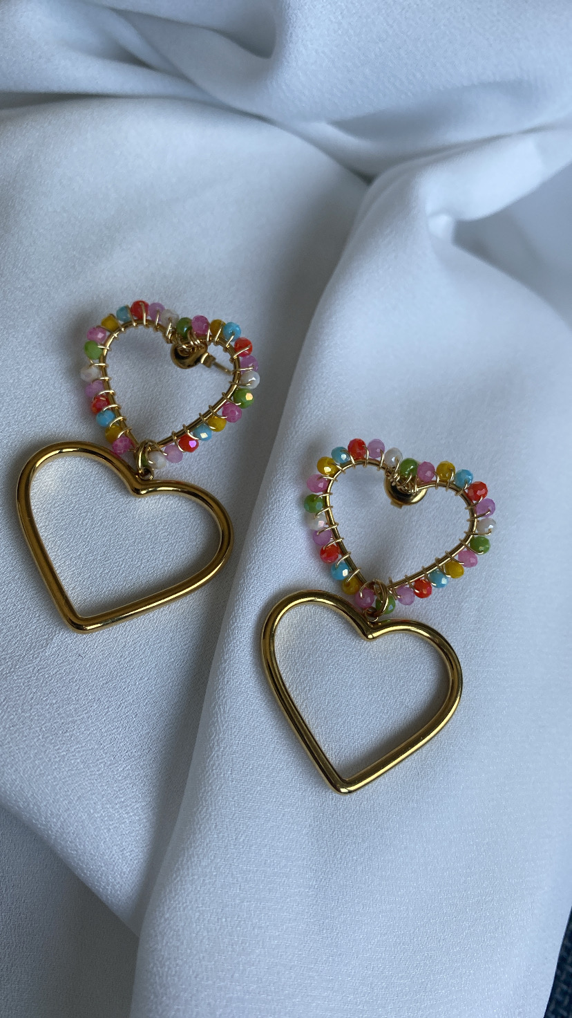 Brincos de coração dourados com contas coloridas sobre tecido branco
