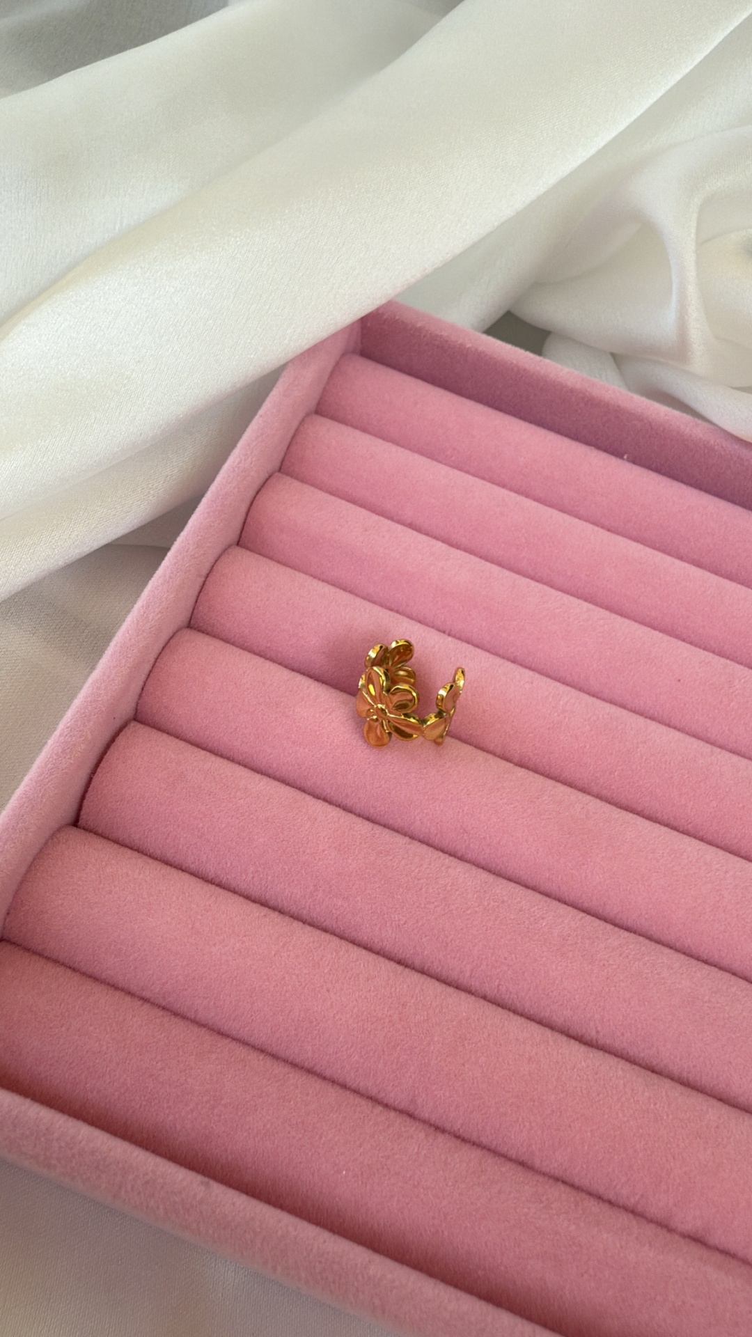 Anel dourado com design de folhas numa caixa rosa para anéis