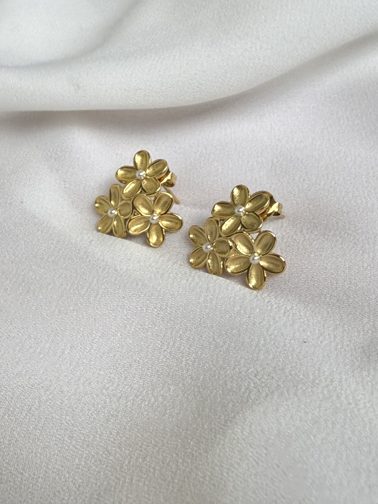 Brincos dourados em forma de flores com pequenas pedras no centro