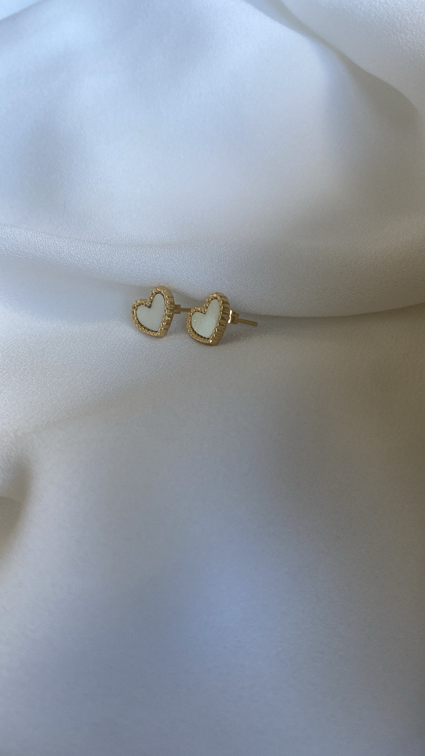 Brincos de coração dourados com interior branco sobre tecido branco.
