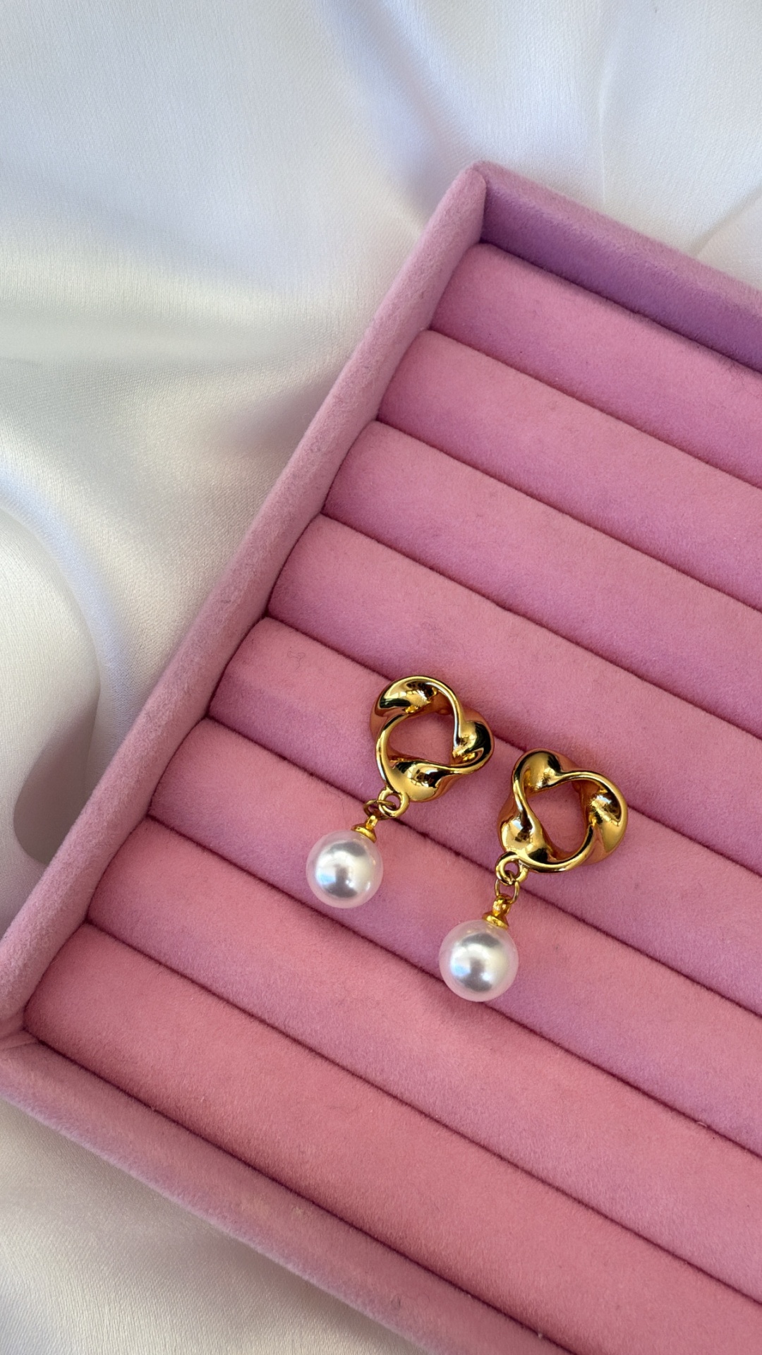 Brincos dourados com pedra branca num estojo rosa em tecido aveludado