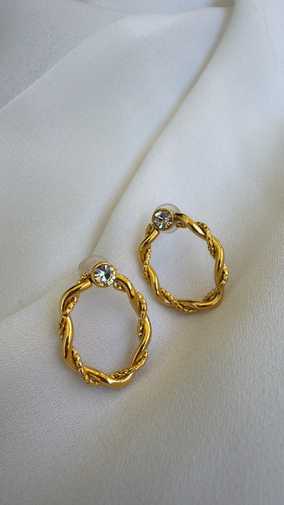 Brincos dourados em forma de argola com pedra brilhante em tecido branco